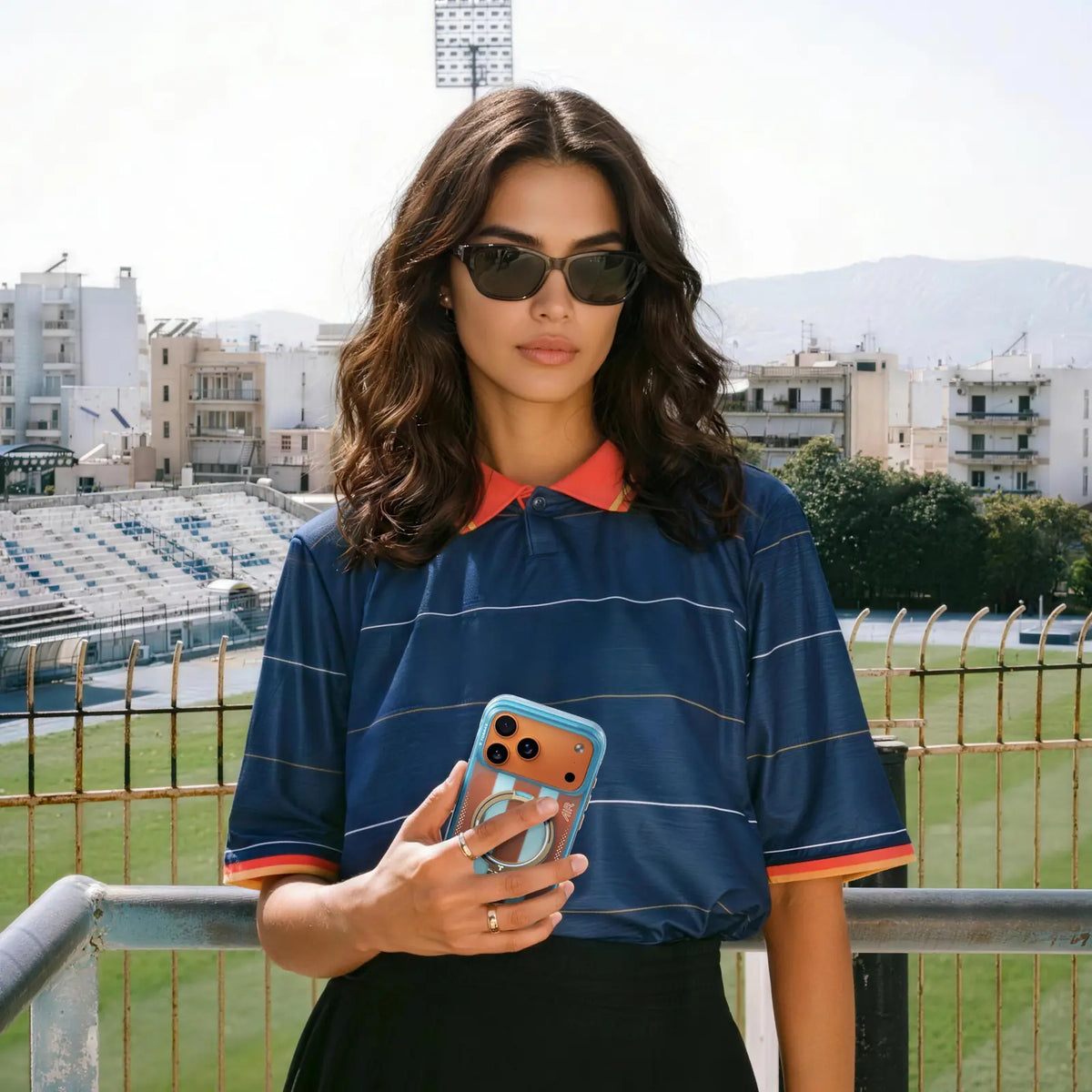Woman by a football pitch holding a phone in a light blue TORRAS case